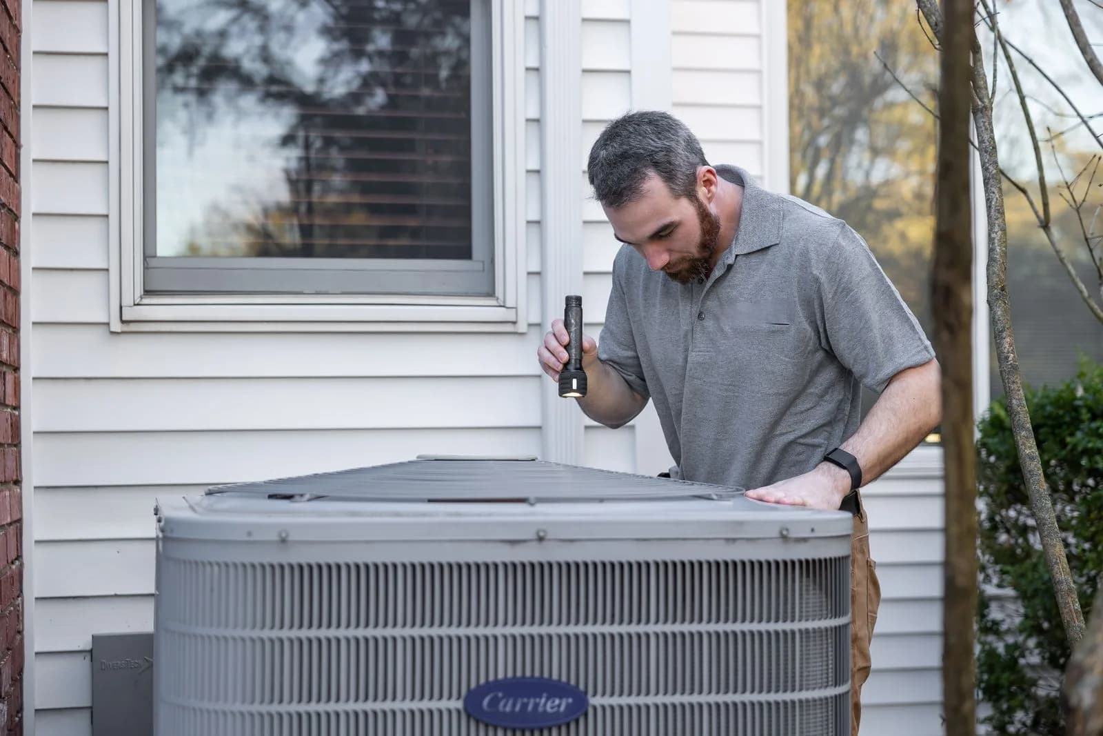 HVAC technician inspecting an outdoor air conditioning condenser beside a house