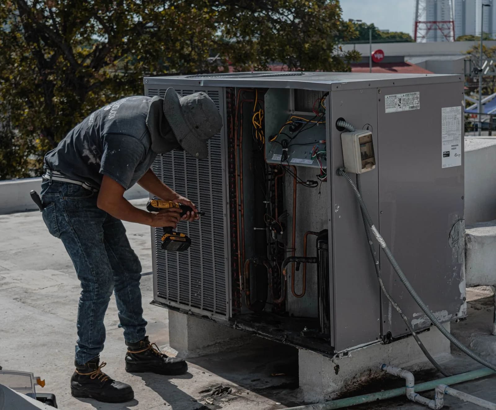 Technician servicing an open rooftop package HVAC unit on a commercial building roof