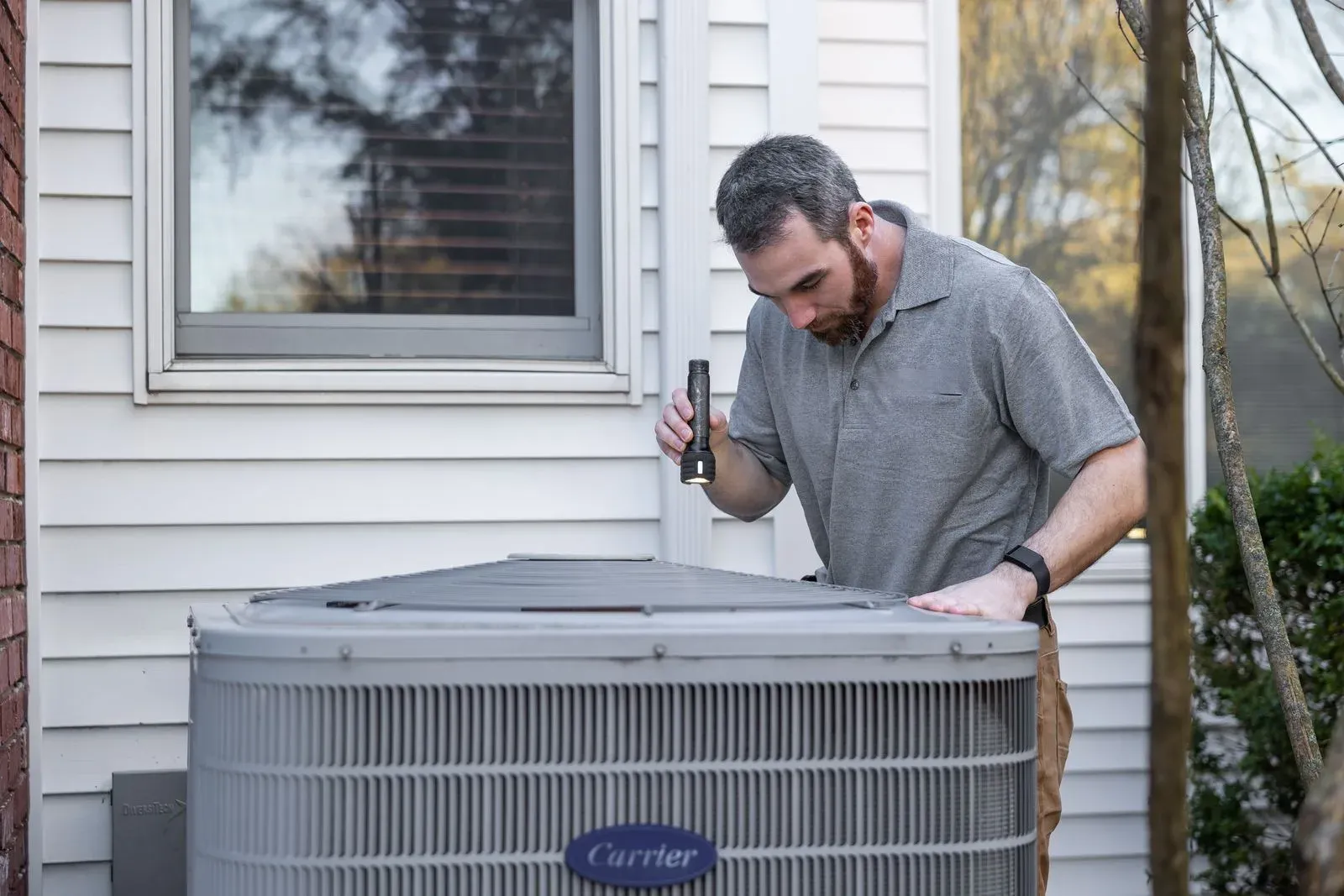 HVAC technician inspecting an outdoor air conditioning condenser beside a house