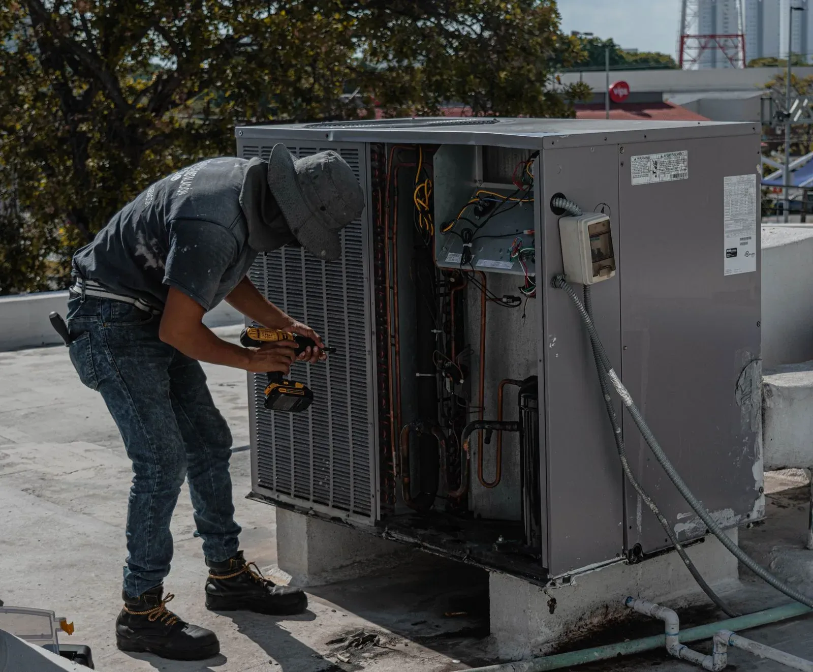 Technician servicing an open rooftop package HVAC unit on a commercial building roof